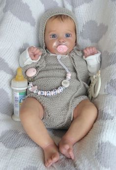 a baby doll with a pacifier in it's mouth sitting on a blanket