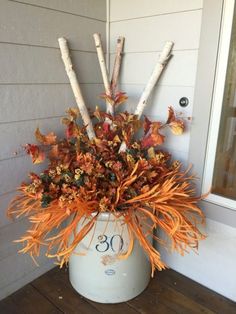 an arrangement of branches and leaves in a bucket on the front porch for fall decor