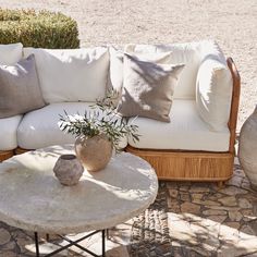 a white couch sitting next to a wooden table on top of a stone floor covered in pillows