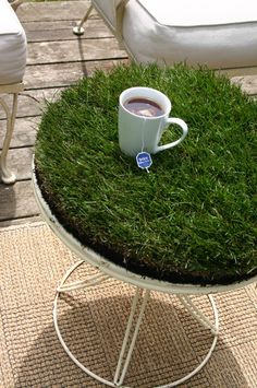 a cup of coffee sitting on top of a table covered in green grass next to a white chair