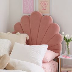 a bed with pink headboard and pillows on top of it next to a vase filled with flowers