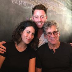 three people posing for a photo in front of a chalkboard with writing on it