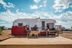 three people and a dog sitting on a picnic table in front of a trailer