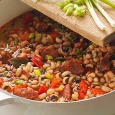 a pot filled with beans and vegetables next to a wooden spoon