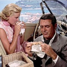 a man and woman sitting in a car while eating food from paper napkins on the table