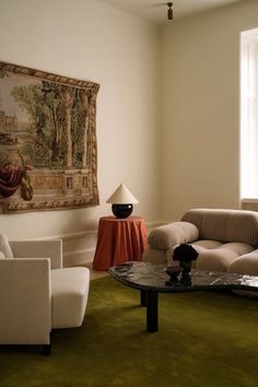 a living room filled with furniture and a painting on the wall above it's glass top coffee table