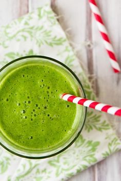 a green smoothie in a glass with two straws next to it on a napkin