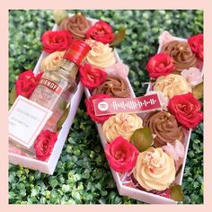 two heart shaped boxes filled with cupcakes next to a bottle of alcohol and flowers