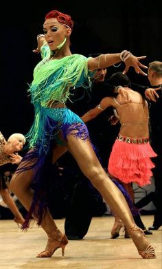 a woman is dancing on the dance floor with other people around her and wearing colorful clothing