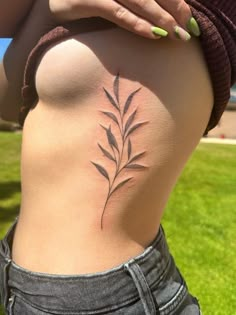 a woman's stomach with a small plant tattoo on her side ribcage