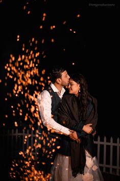 a man and woman standing next to each other in front of a fence with fire