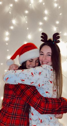 two girls hugging each other with christmas lights in the back ground behind them, and one girl wearing a santa's hat on her head