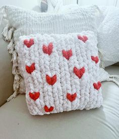 a white crocheted pillow with red hearts on it sitting on a gray couch