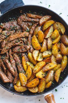 steak and potatoes in a skillet on a white surface with parsley sprigs