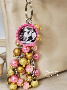 a pink and gold key chain with a picture on it's side, hanging from a beige bag