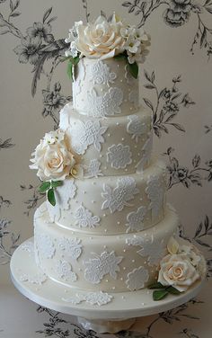 a three tiered wedding cake with white flowers on the top and bottom, sitting on a table