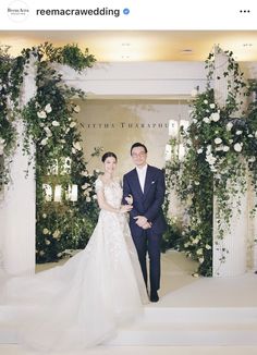 a man and woman standing next to each other in front of an arch covered with flowers