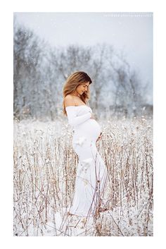 a pregnant woman standing in the snow with her hands on her hips, wearing a white dress