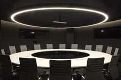 a round conference table with chairs around it in a dark meeting room, lit by recessed lights