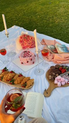 a table full of food and drinks on top of a white cloth covered picnic blanket