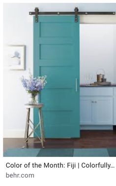 an open blue door in a kitchen next to a stool and table with flowers on it