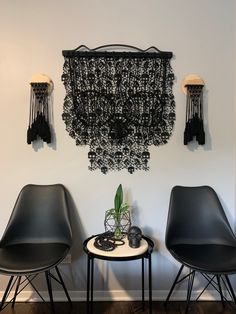 two black chairs sitting next to each other in front of a wall hanging with beads on it