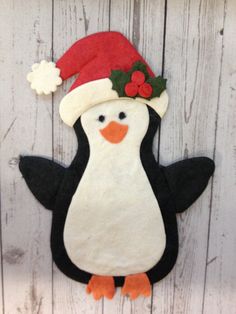 a felt penguin with a santa hat on it's head, standing against a wooden wall