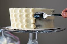 a person is holding a spoon over a cake on a plate with white frosting