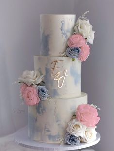 a three tiered wedding cake with flowers on the top and initials on the side