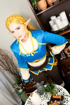 a woman dressed in a blue and yellow outfit standing next to a shelf with plants