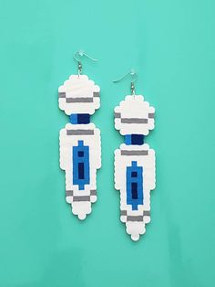 a pair of earrings made out of legos on a green background with blue and white beads