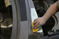 a man polishing the front part of a car with a yellow cloth on it