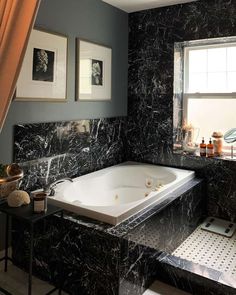 a bathroom with black marble walls and flooring is pictured in this image, there are pictures on the wall above the bathtub