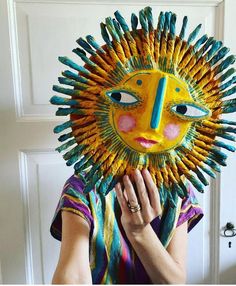 a woman holding up a sun mask made out of crayons