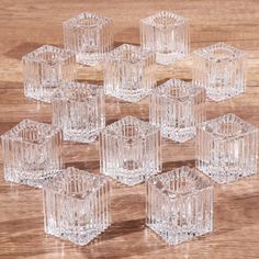 six clear glass candlesticks sitting on top of a wooden table next to each other