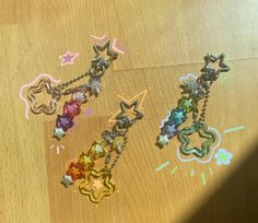 three different colored stars are hanging from chains on a wooden table with other items in the background