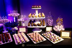 an assortment of cupcakes and desserts displayed on trays in front of purple lighting