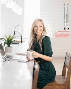 a woman sitting at a table with a laptop and coffee mug in her hand, smiling