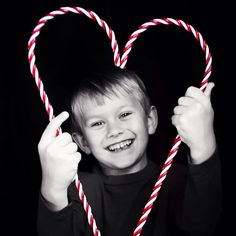 a young boy holding two candy canes in the shape of a heart