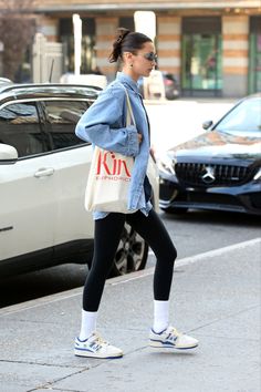 a woman in black leggings and sneakers is walking down the street with a tote bag