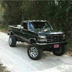 a black pickup truck parked on the side of a dirt road in front of trees