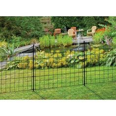 a black fence is in the middle of a green yard with chairs and flowers around it