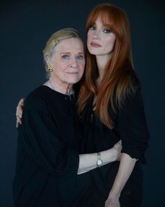 two women are hugging each other in front of a black background and one has long red hair