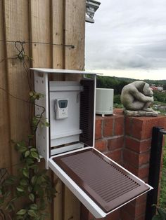 an open box on the side of a brick building with a statue in the background