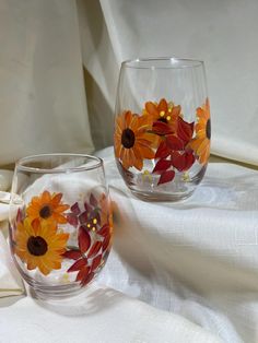 two glasses with painted flowers on them are sitting on a white cloth covered tablecloth