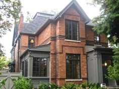 a large brick house with lots of windows and bushes in front of the house on a cloudy day