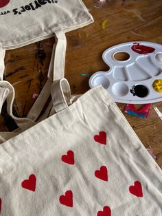 two bags with hearts painted on them sitting on a table next to paintbrushes