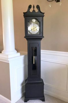 a black grandfather clock sitting in the corner of a room next to a white column