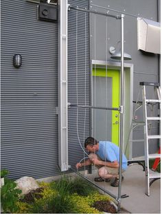 a man is working on the side of a building with green doors and ladders