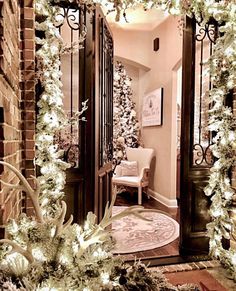 a hallway decorated for christmas with white lights and greenery on the door, surrounded by brick pillars